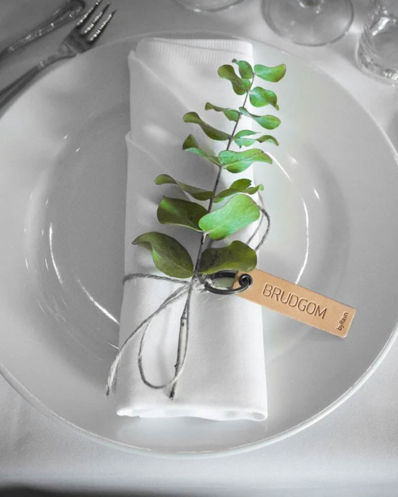 MERRY leather place card in natural with the engraving "Brudgom" tied around a white napkin with green sprig on a plate
