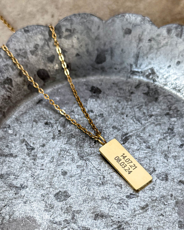 MIO necklace in gold-plated stainless steel with the dates "14.07.21 08.03.24" engraved on rectangular pendant, on a wavy-edged zinc tray
