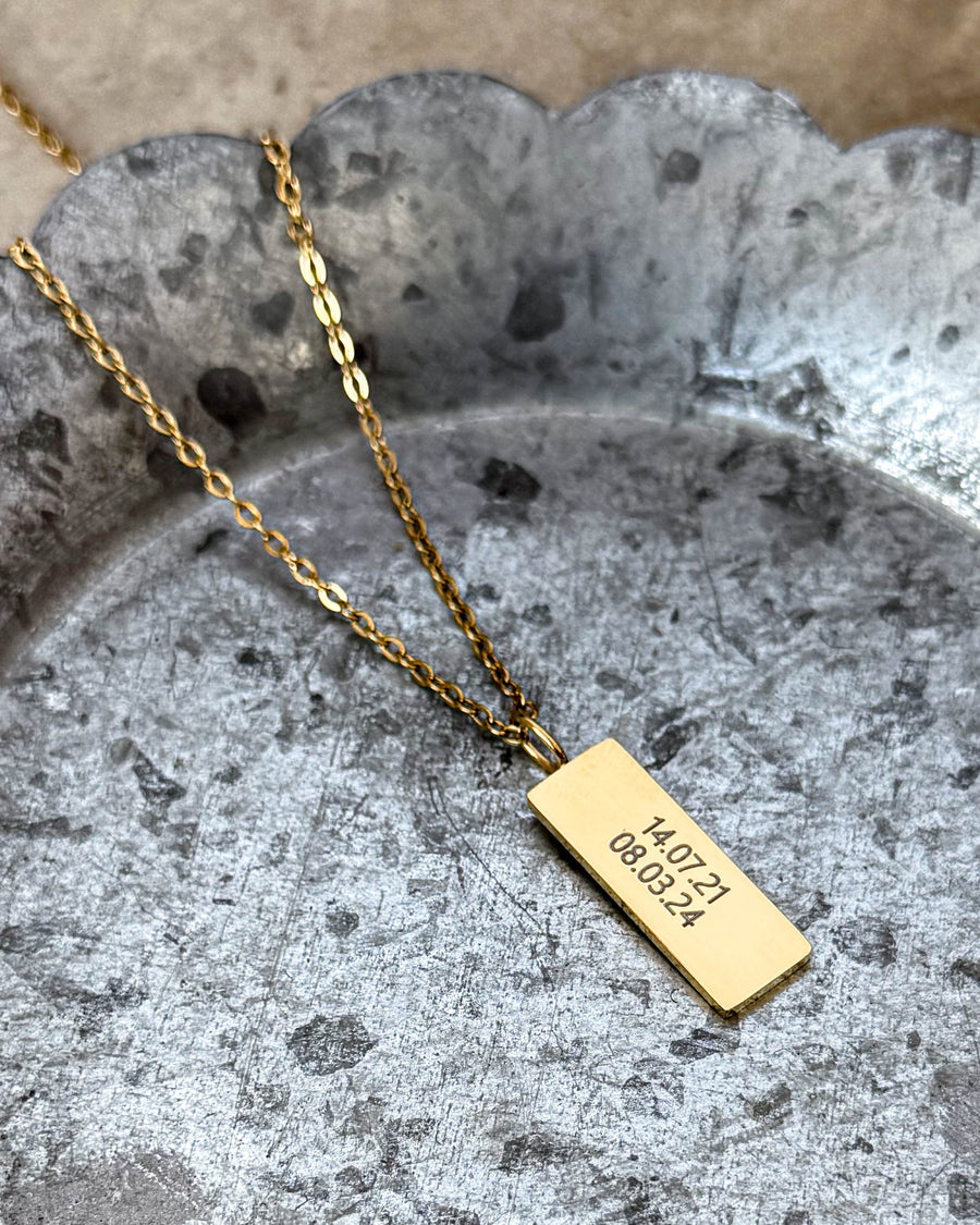 MIO necklace in gold-plated stainless steel with the dates "14.07.21 08.03.24" engraved on rectangular pendant, on a wavy-edged zinc tray