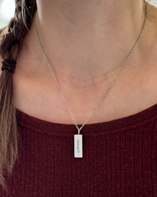 MIO necklace in silver-coloured stainless steel with "I love you" ♡ engraved on rectangular pendant, worn around the neck over burgundy top