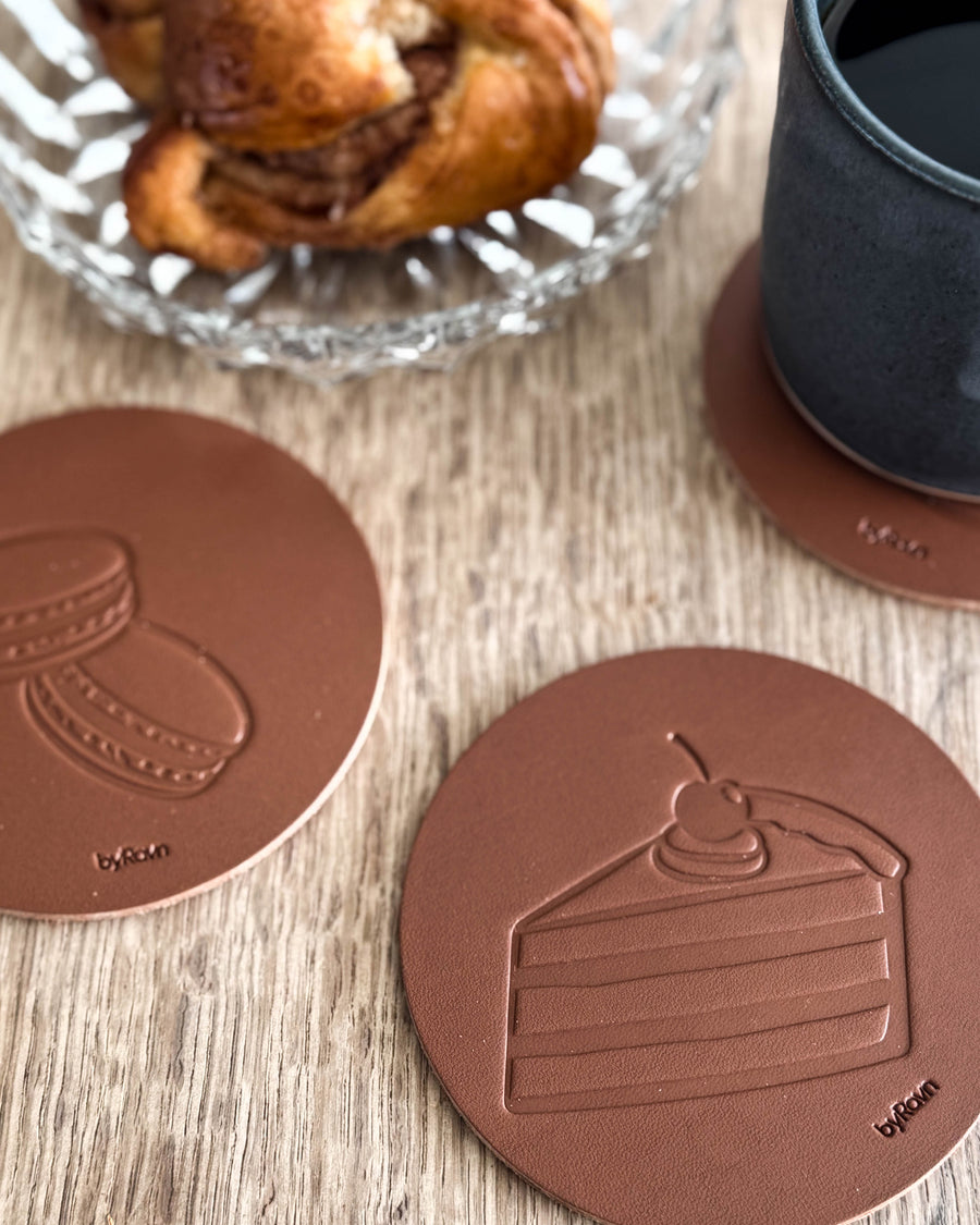 MOKKA coffee & cake coasters in cognac leather embossed with layer cake and macarons on a wooden table by cinnamon bun and black cup