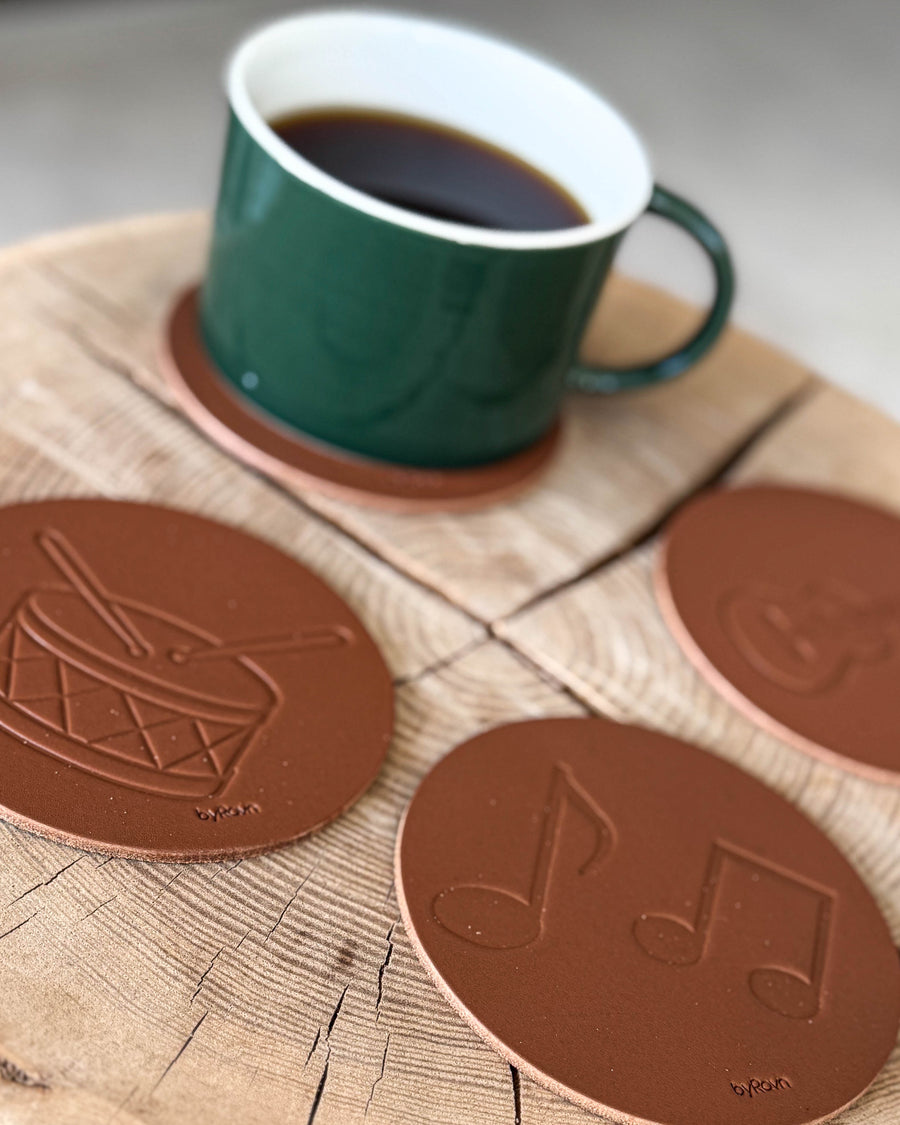 MOKKA music coasters in cognac leather embossed with drum and sheet music on a wood slice with a green coffee cup
