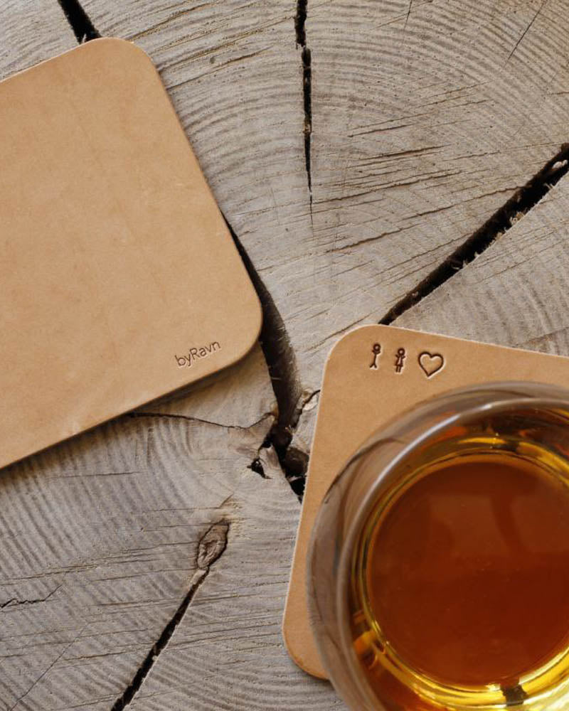 MOKKA square coasters in natural leather embossed with matchstick family and heart, with a tea glass on a wooden slice