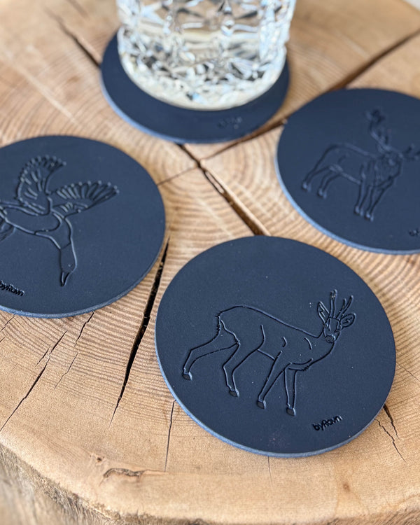 MOKKA hunting coasters in navy blue leather embossed with roebuck, mallard and red deer stag on a wooden slab by a crystal glass