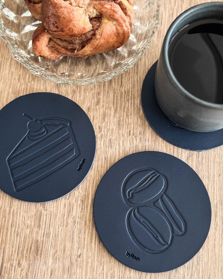 MOKKA coffee & cake coasters in navy blue leather embossed with layer cake and coffee beans on a wooden table by cinnamon bun and grey cup