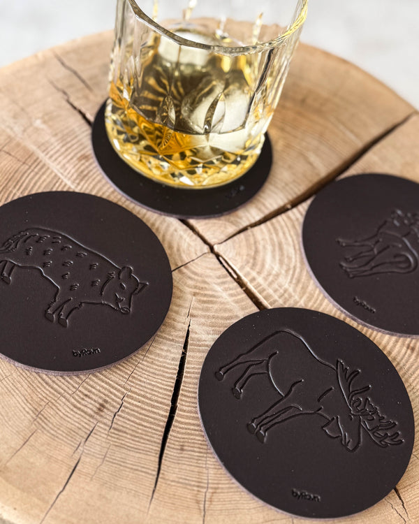 MOKKA hunting coasters in dark brown leather embossed with wild boar, elk and fallow deer on a wooden slab by a whisky glass