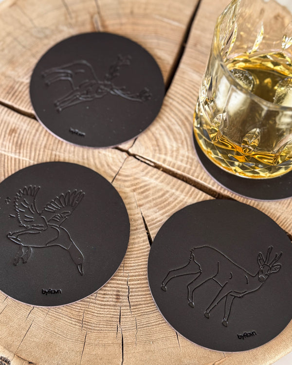 MOKKA hunting coasters in dark brown leather embossed with mallard, roebuck and red deer stag on a wooden slab by a whisky glass