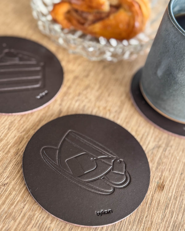 MOKKA coffee & cake coasters in dark brown leather embossed with teacup and layer cake on a wooden table by cinnamon bun and green cup