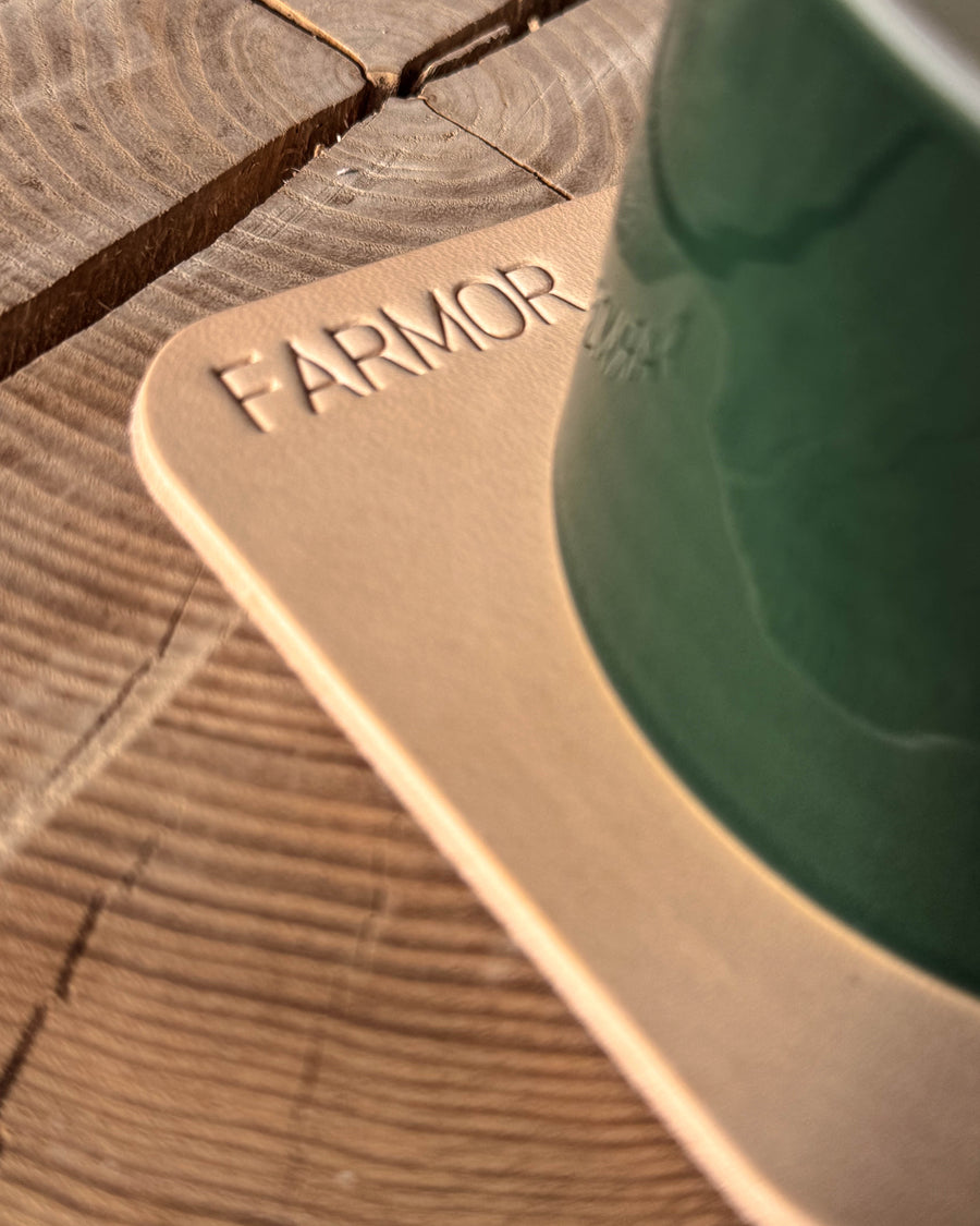 MOKKA square coaster in natural leather with the engraving "Farmor" under a green ceramic cup on a wooden slice