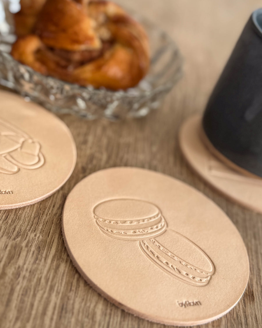 MOKKA coffee & cake coaster in natural full-grain leather embossed with macarons on a wooden table by cinnamon bun and black cup
