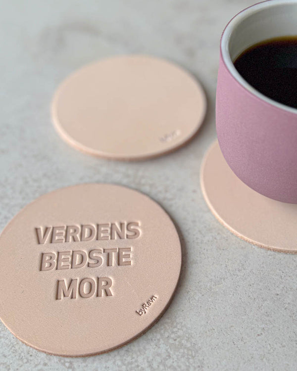 MOKKA coasters in natural leather embossed "Verdens bedste mor" on a light table with a pink coffee cup
