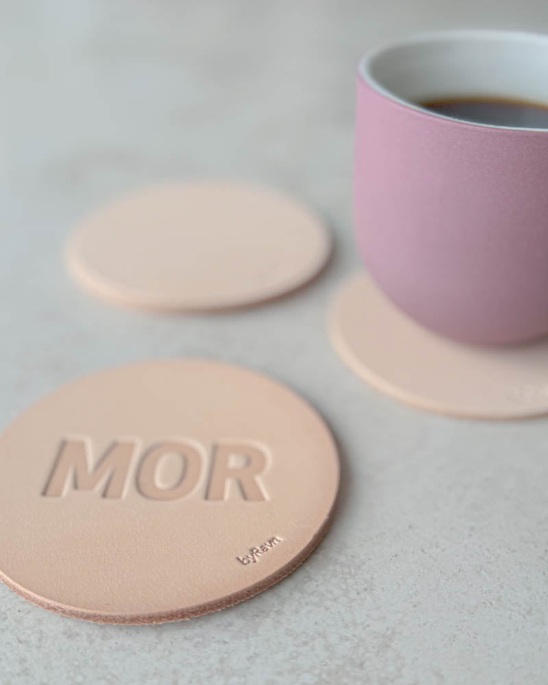 MOKKA coaster in natural full-grain leather embossed "Mor" in capital letters, pink coffee cup on a coaster behind