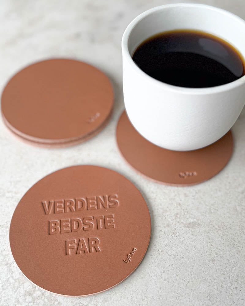 MOKKA coasters in cognac leather embossed "Verdens bedste far" on a light table with a white coffee cup