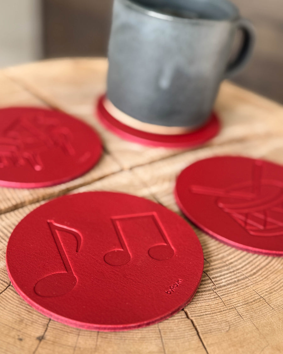 MOKKA music coasters in red leather embossed with sheet music, grand piano and drum on a wooden table with a grey ceramic cup