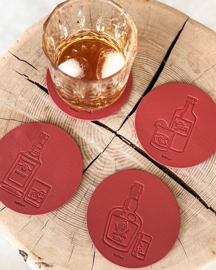 MOKKA spirits coasters in red leather embossed with whisky, gin and rum on a wood slice by a crystal glass of whisky and ice