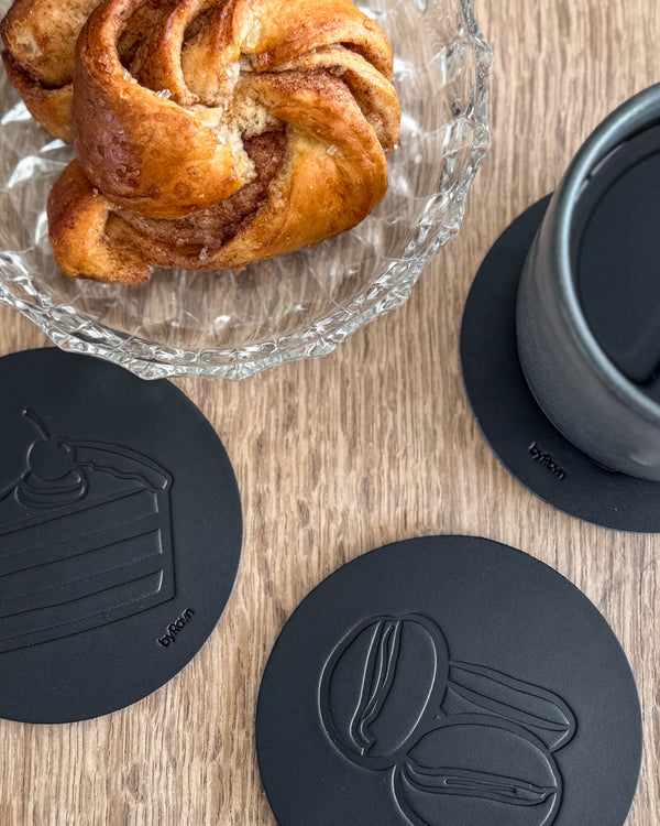 MOKKA coffee & cake coasters in black leather embossed with layer cake and coffee beans on a wooden table by cinnamon bun and grey cup