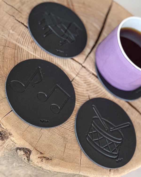 MOKKA music coasters in black leather embossed with sheet music, drum and grand piano on a wood slice with a purple coffee cup