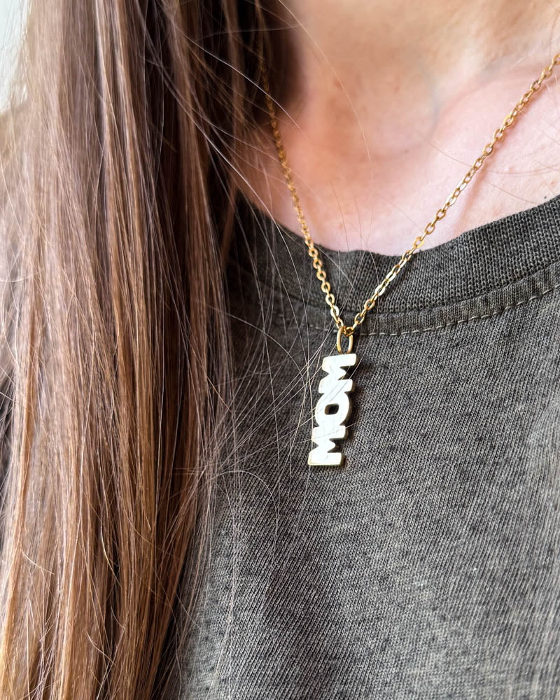 MOM necklace with "MOM" letter pendant, shown here in gold-plated stainless steel, worn around the neck over a grey t-shirt