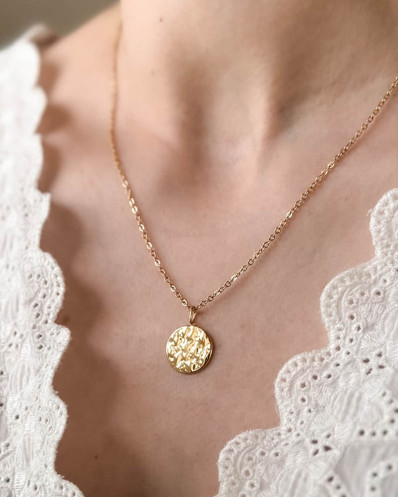 MOON QUOTE necklace in gold-plated stainless steel with hammered round coin facing out, worn around the neck over a white lace top