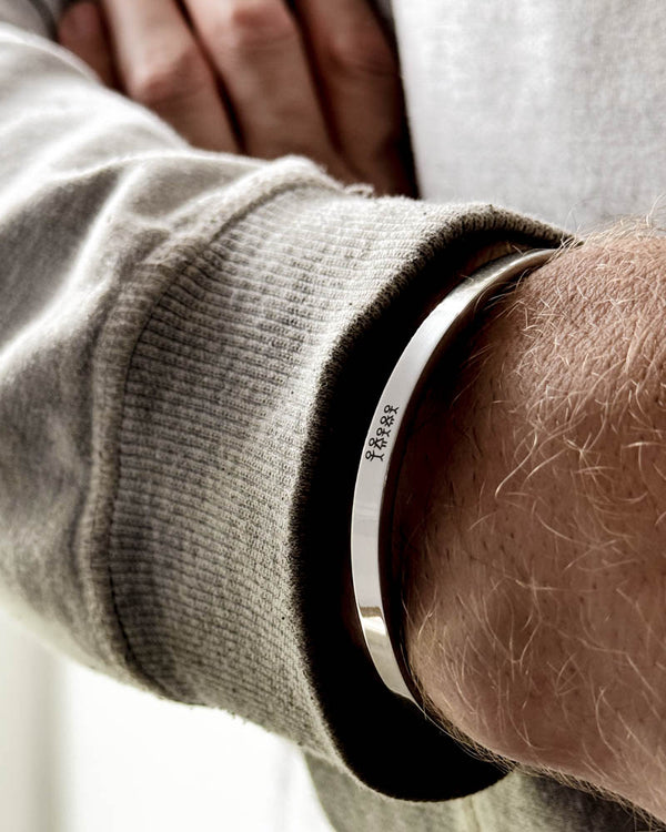 MARS STICK bracelet in silver-coloured stainless steel with engraved matchstick family on a man's wrist, light grey sweatshirt