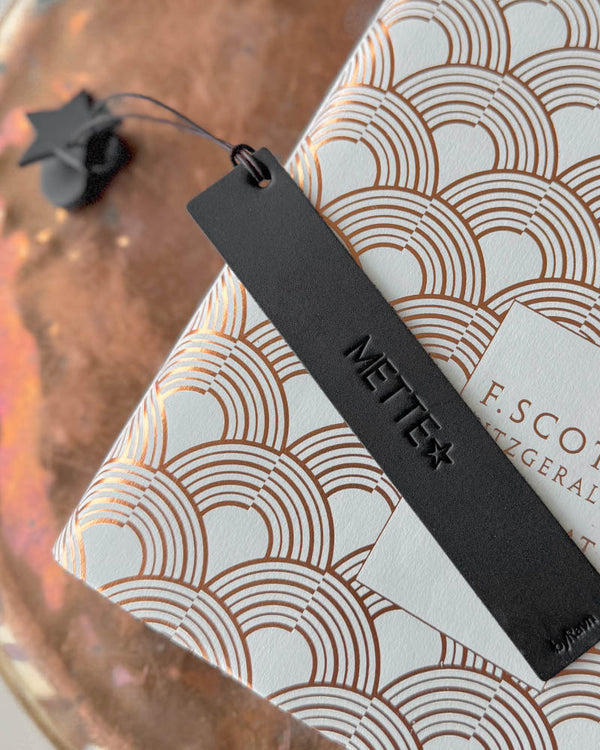 PAGE bookmark in black leather with the name "Mette" and a star engraved on a book with copper pattern on a copper tray