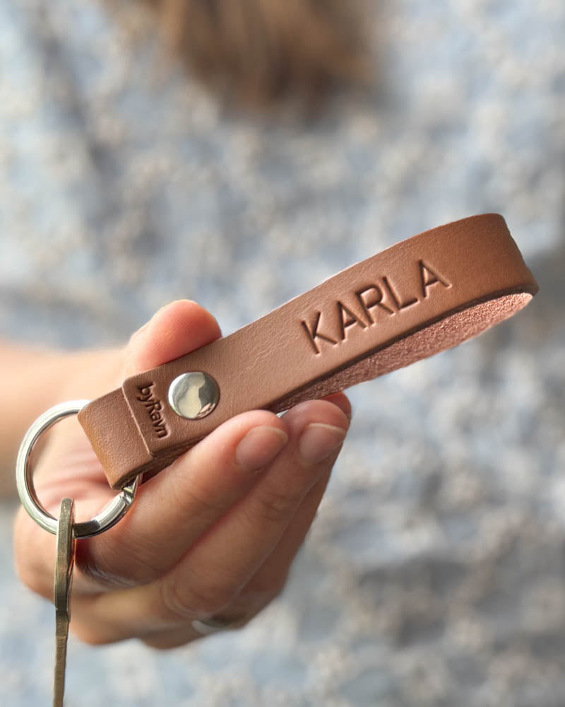 RAVN leather keyring in cognac with the name "Karla" engraved, held in hand
