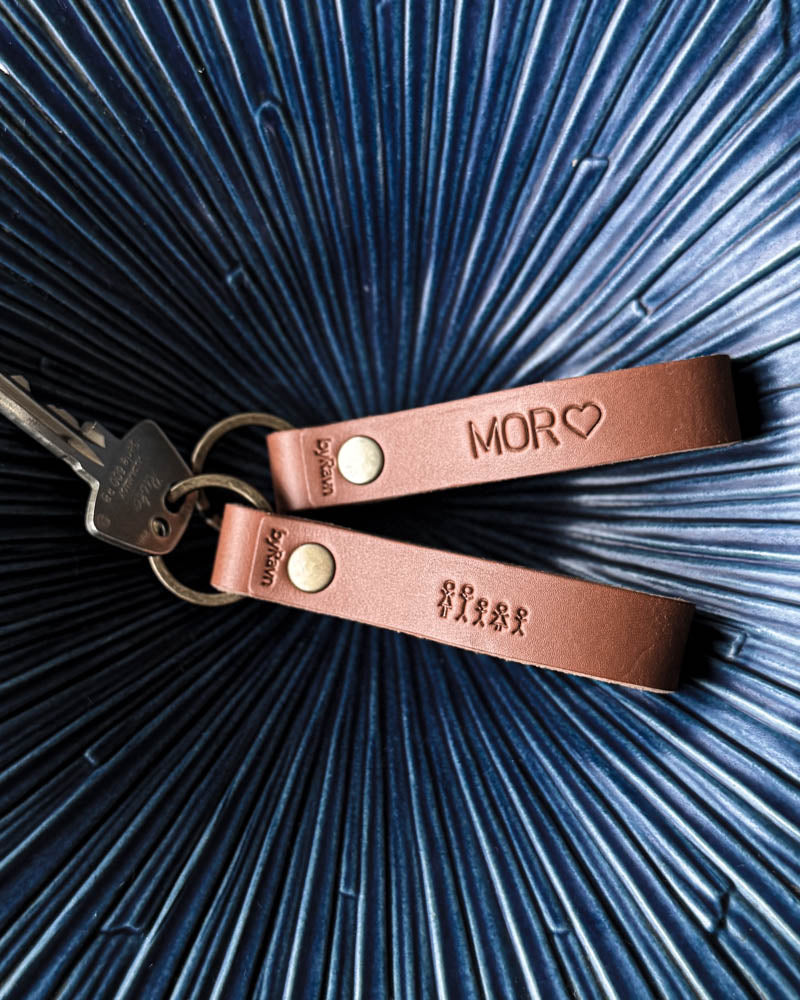 Two RAVN leather keyrings in cognac with the engraving "Mor" ♡ and matchstick family, with keys in a blue ribbed bowl