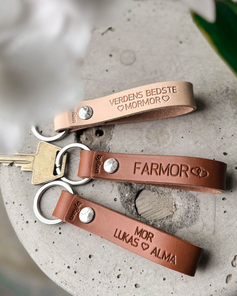 Three RAVN leather keyrings in natural and cognac with "Verdens bedste mormor", "Farmor" and "Mor Lukas ♡ Alma" engraved, on concrete