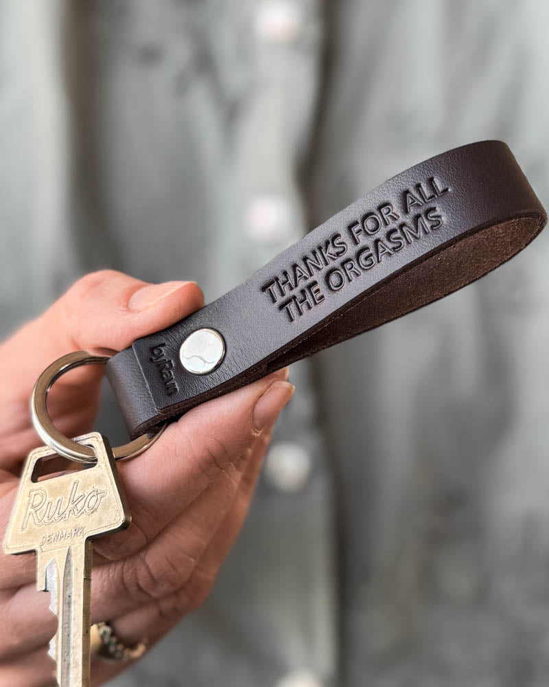 RAVN leather keyring in dark brown with the engraving "Thanks for all the orgasms", held in hand with keys