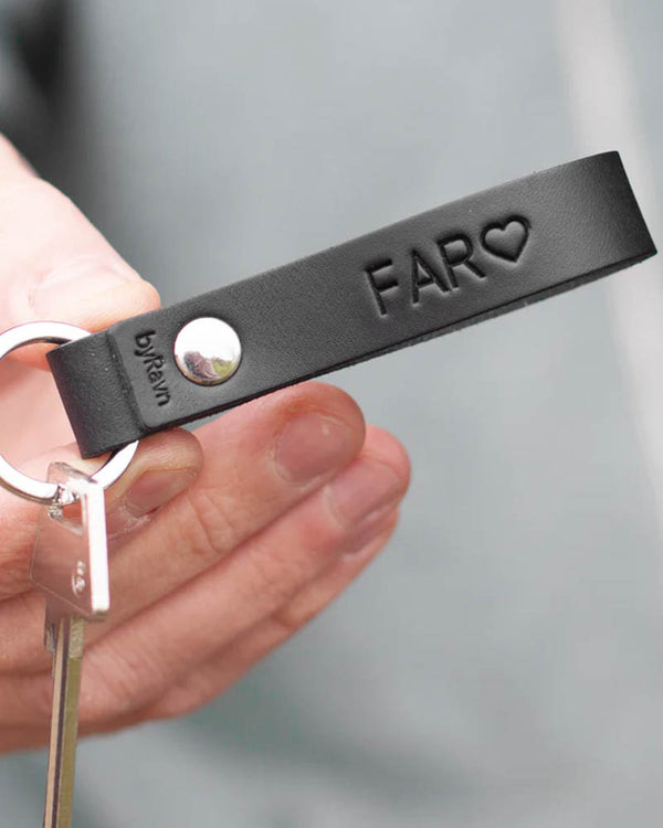 RAVN leather keyring in black with the engraving "Far" ♡ and steel rivet, held in hand with key