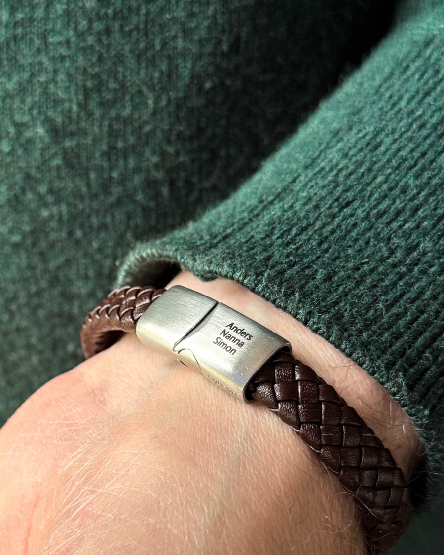 RAY leather bracelet in dark brown braided leather with the names "Anders, Nanna, Simon" engraved on the steel clasp, worn with a green knit