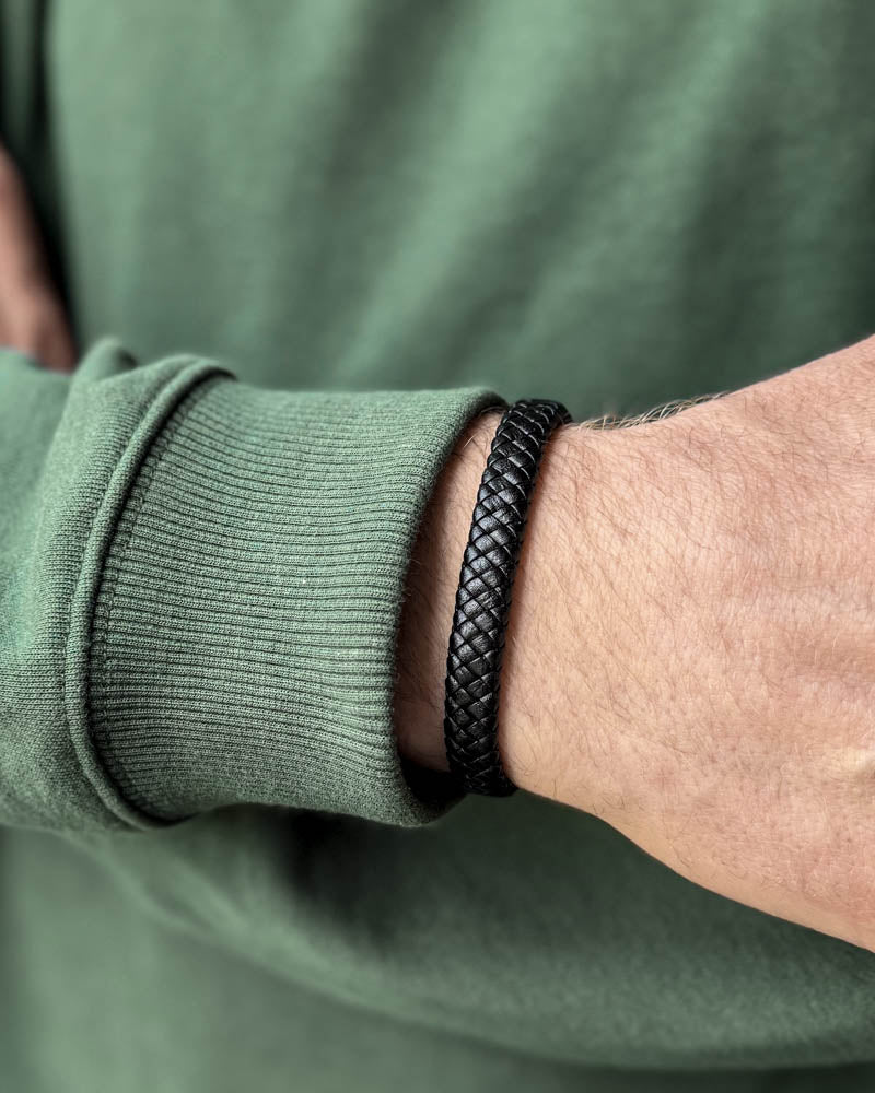 RAY leather bracelet in black braided leather worn on a man's wrist, green sweatshirt