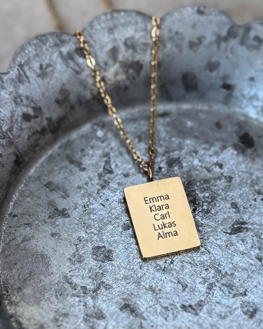 RAZ name necklace in gold-plated stainless steel with names "Emma Klara Carl Lukas Alma" engraved on rectangular plate, on zinc tray