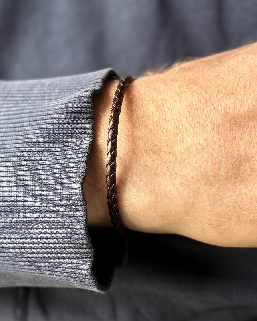 RIO leather bracelet in dark brown braided leather on a man's wrist, blue-grey sweatshirt
