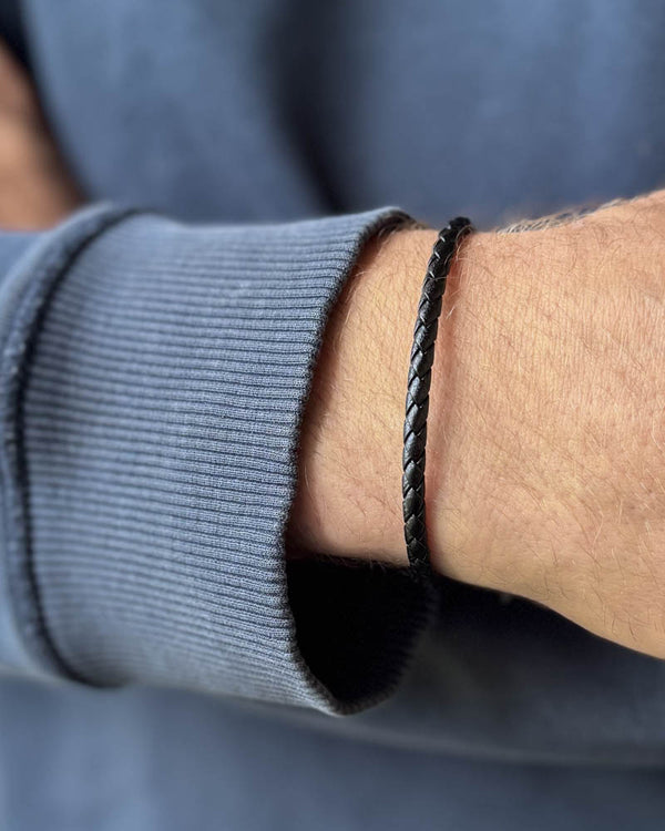 RIO leather bracelet in black braided leather worn on a man's wrist, blue-grey sweatshirt