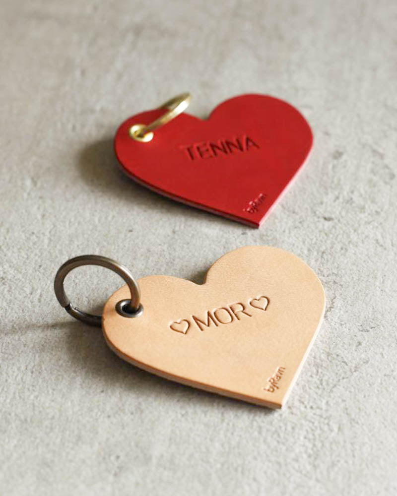 ROSE heart-shaped keyrings in natural and red leather with the engravings ♡ "Mor" ♡ and "Tenna" on a light concrete background