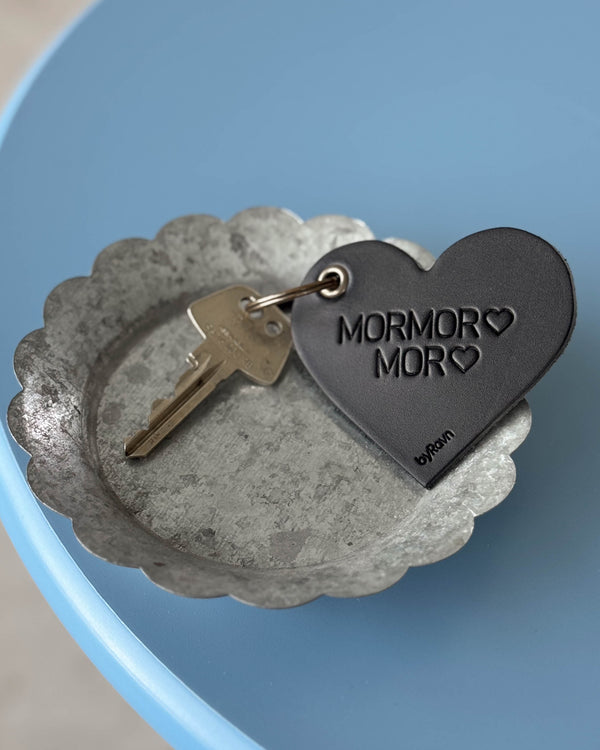 ROSE heart keyring in black leather with the engraving "Mormor ♡ Mor ♡" and key in a zinc bowl on a blue table