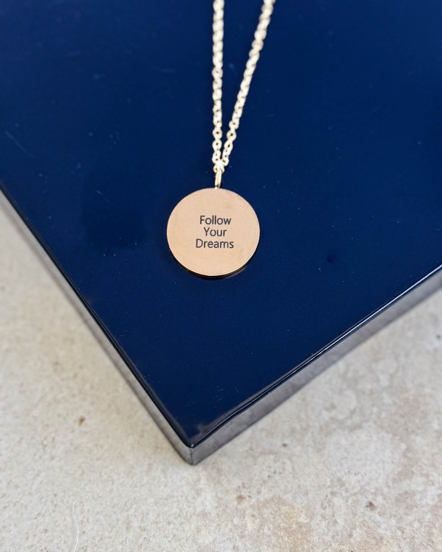 SIA QUOTE necklace in gold-plated stainless steel with the engraving "Follow your dreams" on a round pendant, on a navy blue box