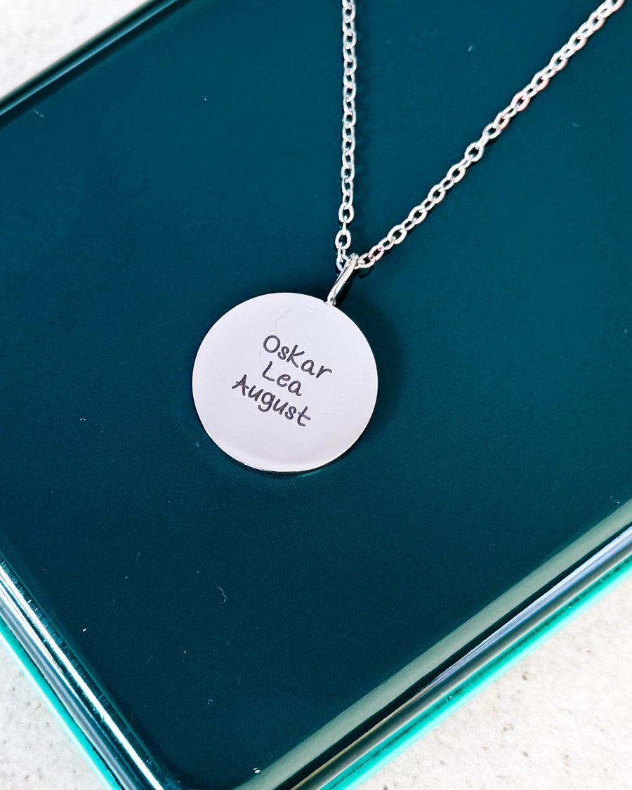 SIA QUOTE SCRIPT name necklace in silver-coloured steel with the names "Oskar Lea August" in handwriting, on a green glass box