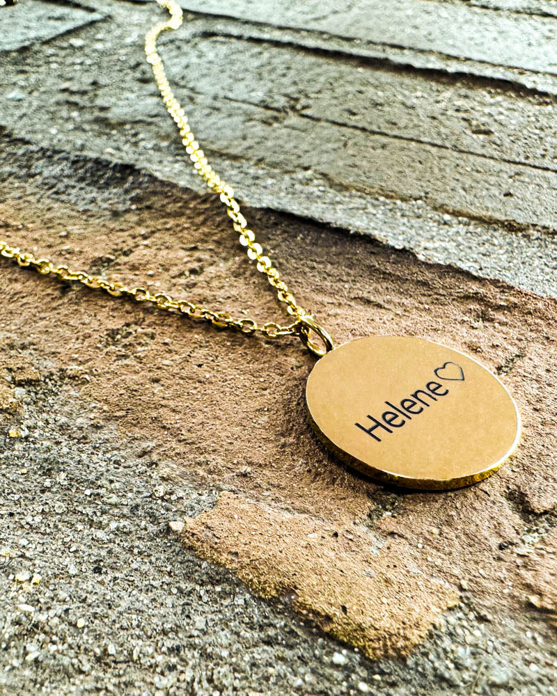 SIA NOTE name necklace in gold-plated stainless steel with the name "Helene" ♡ engraved, lying on a brick wall