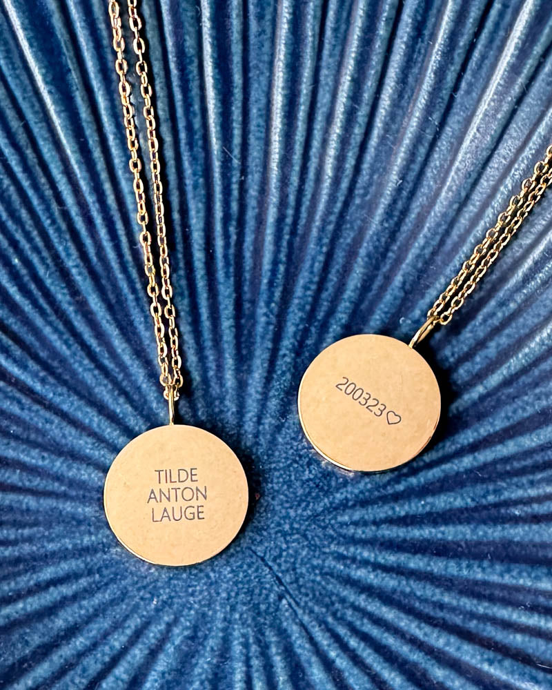 SIA QUOTE name necklace in gold-plated stainless steel, two pendants engraved "Tilde Anton Lauge" and "200323" ♡, on a blue ribbed bowl