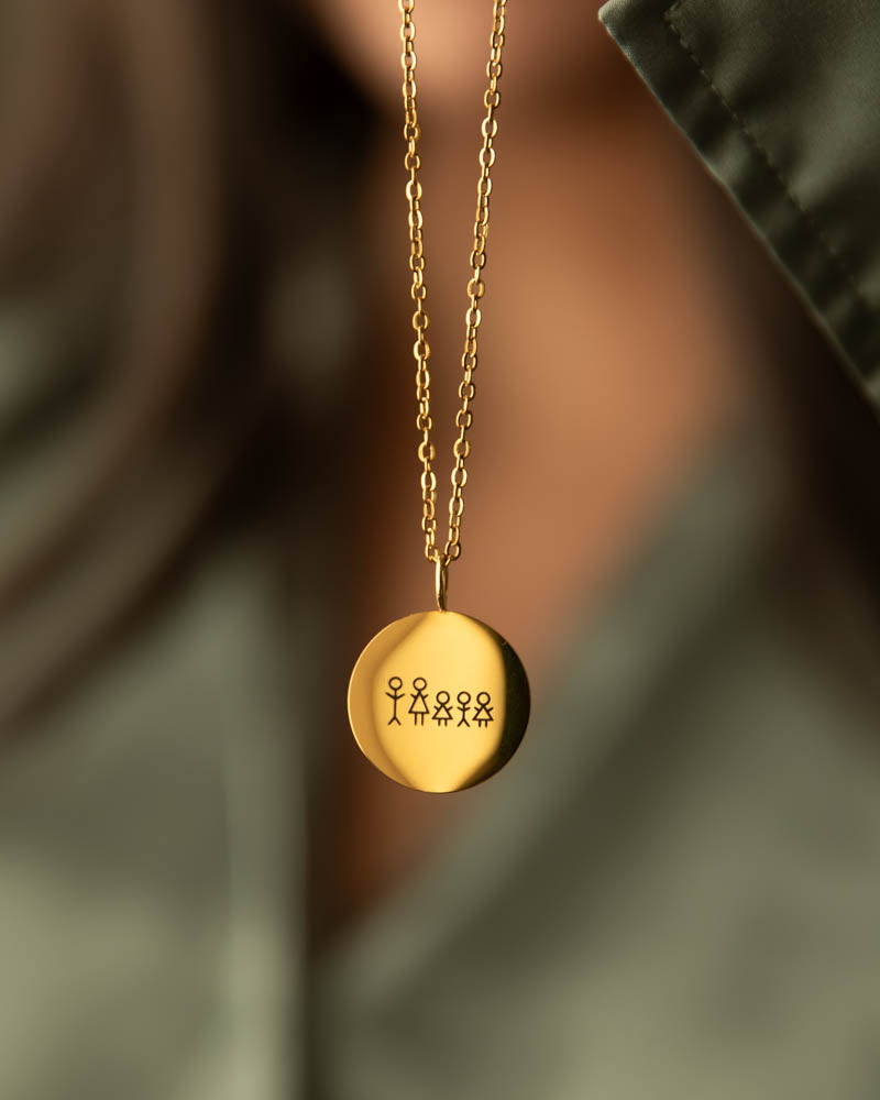 SIA STICK necklace in gold-plated stainless steel engraved with a matchstick family of five, worn around the neck over a green shirt