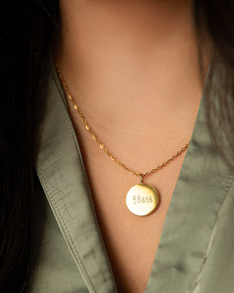 SIA STICK necklace in gold-plated steel with a matchstick family engraved on a round pendant, worn around the neck with a green shirt