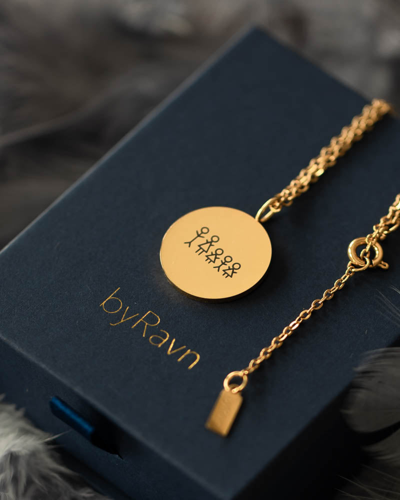 SIA STICK necklace in gold-plated steel engraved with matchstick family and hearts, on a navy blue byRavn gift box with a feather