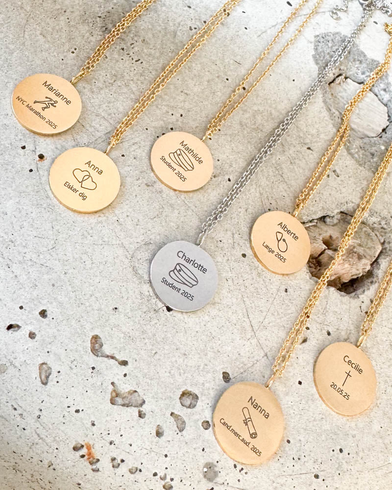 SIA MOMENTS necklaces in silver-coloured and gold-plated steel with names, graduation cap, hearts, cross and diploma, on concrete