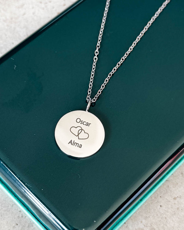 SIA MOMENTS necklace in silver-coloured steel engraved with "Oscar" and "Alma" and two intertwined hearts, on a green glass box