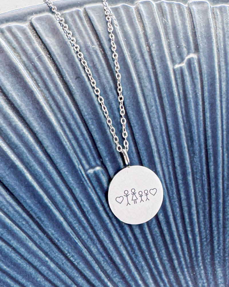 SIA STICK necklace in silver-coloured steel with matchstick family and hearts engraved on a round pendant, on a blue ribbed dish