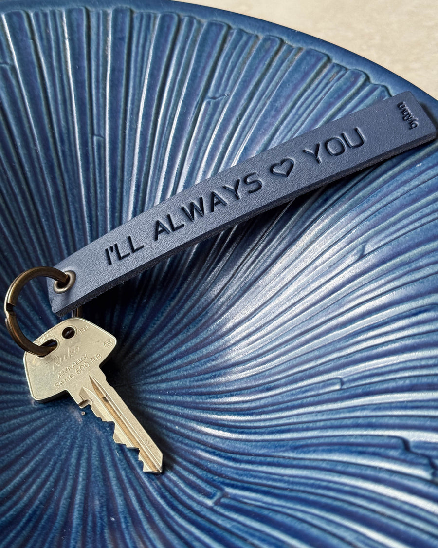 SOLO Large keyring in navy blue leather with the engraving "I'll always ♡ you" and key in a blue ribbed ceramic bowl
