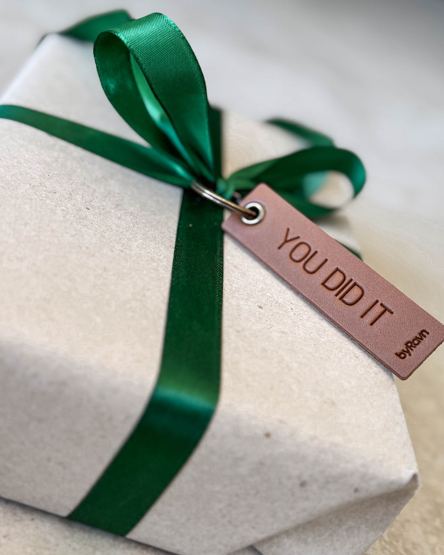 SOLO Small keyring in cognac leather with the engraving "You did it" used as a gift tag on a parcel with green ribbon