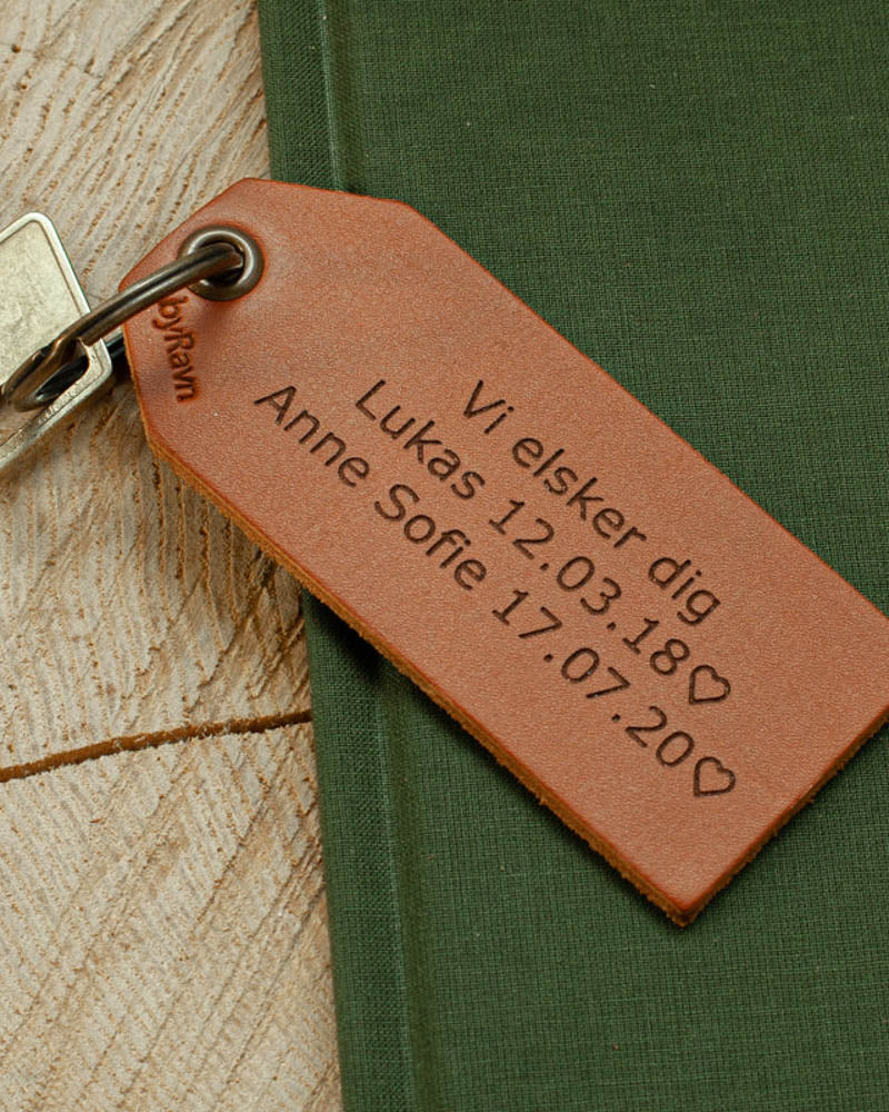 STORM keyring in cognac leather with personalised engraving "Vi elsker dig, Lukas 12.03.18 ♡ Anne Sofie 17.07.20 ♡" on a green book